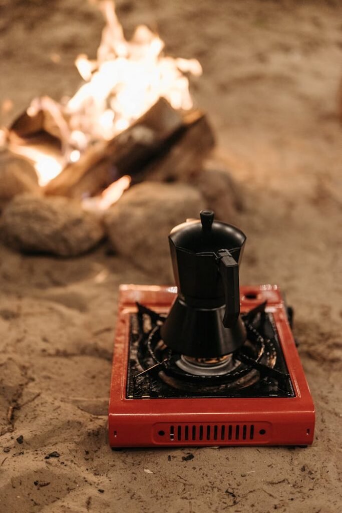 Close-up of a Coffee Pot on a Portable Stove Standing on a Beach near a Campfire